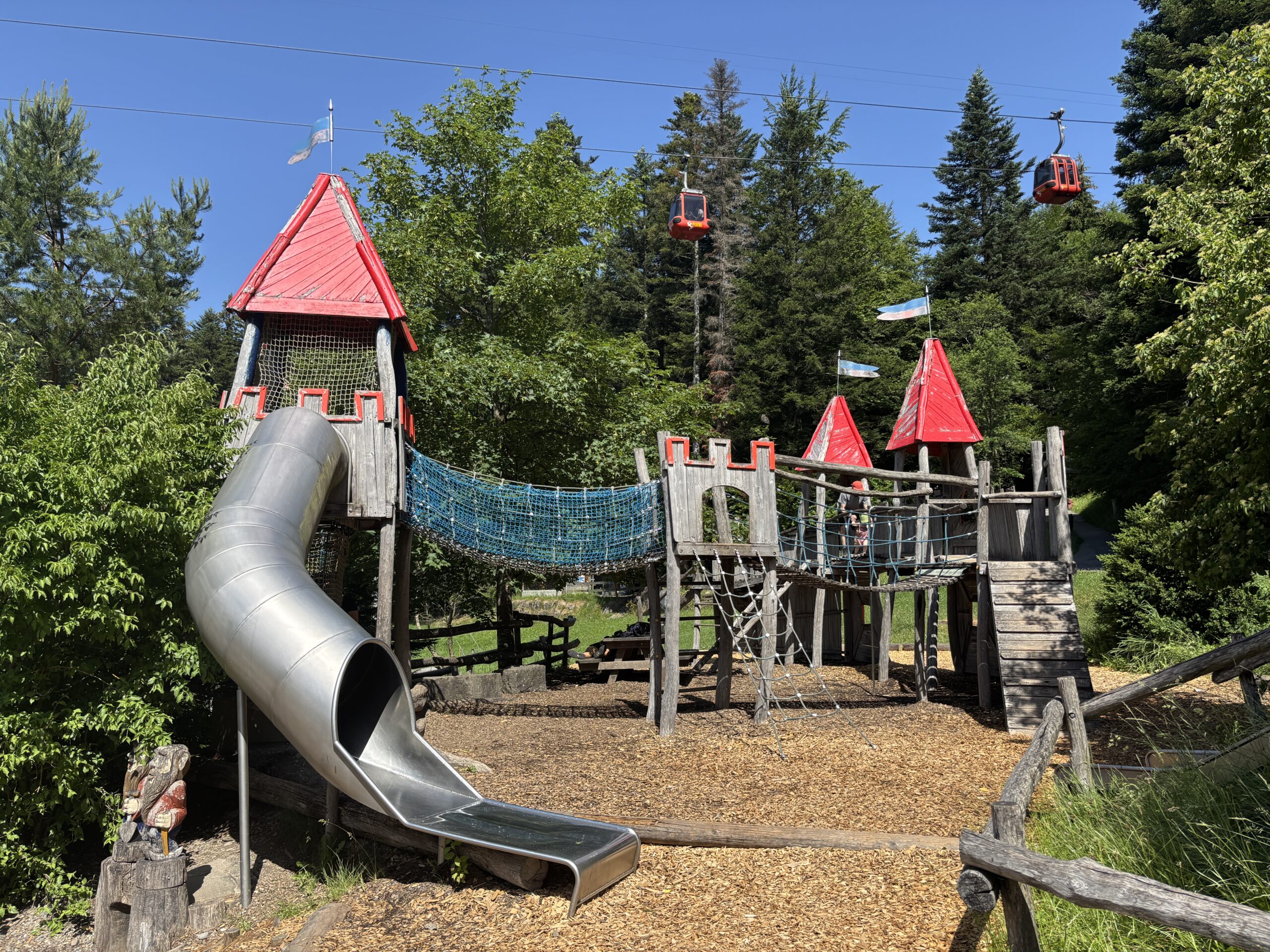 Großer Abenteuerspielplatz bei Krienseregg am Pilatus mit Rutschbahn, Klettergerüst und vorbeifahrenden Gondeln der Panoramabahn.